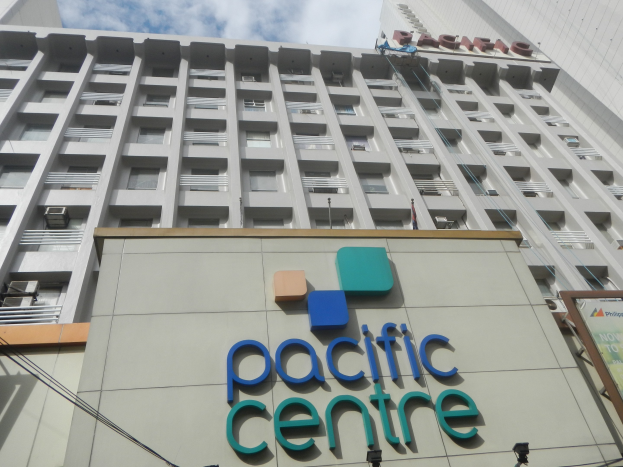 Außensicht des Pacific Centre Hotel in Manila, Philippinen, ein hoher Bau mit Fenstern, Geländern, Klimaanlagen, einem Namensschild, Lampen, Kabeln und Texttafeln vor einem bewölkten Himmel.