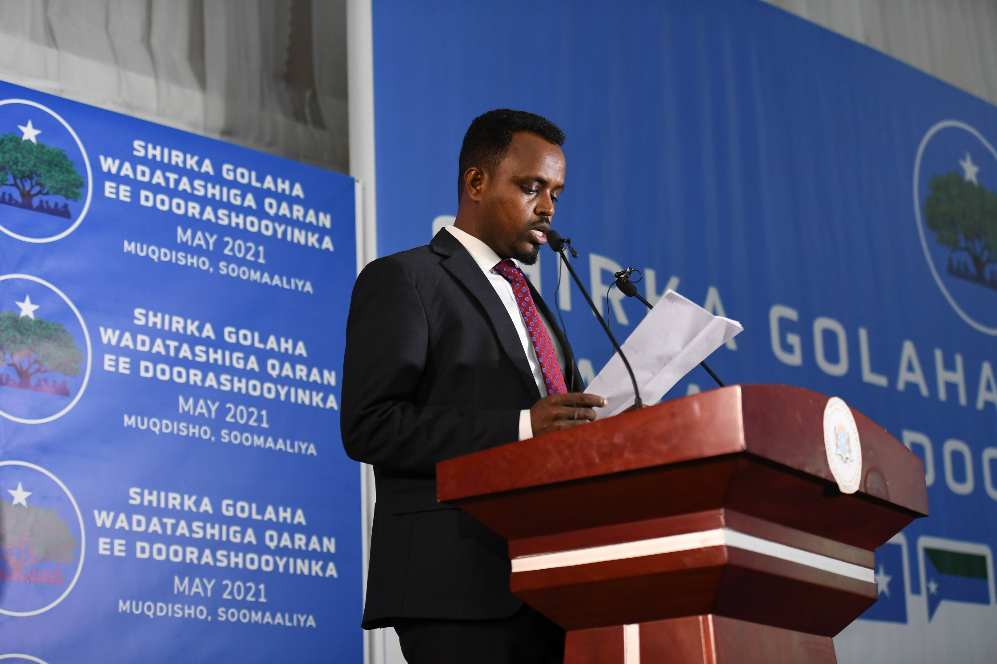 Ein Mann im Anzug spricht an einem Rednerpult mit Papieren in der Hand hinter einem Banner und Vorhängen, wahrscheinlich bei der Ankündigung der neuen Regierung Ghanas.