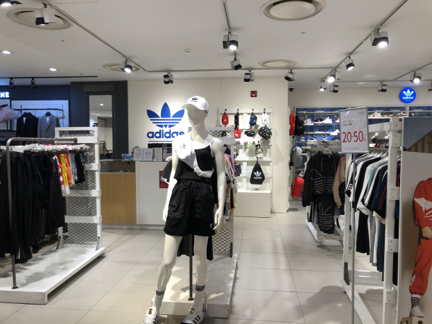 Innenansicht eines adidas-Ladens in Singapur mit Schaufensterpuppen, Kleiderständern, einer Texttafel auf der rechten Seite und Deckenbeleuchtung.