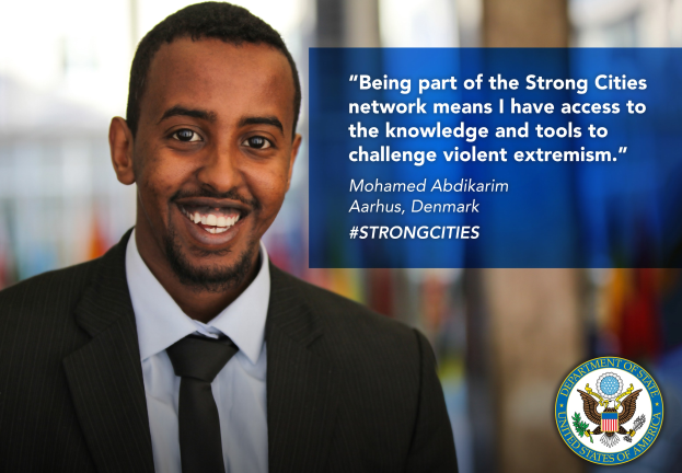 Ein Mann mit einem freundlichen Gesichtsausdruck in einem Anzug und Krawatte steht vor einem unscharfen Hintergrund, mit Text auf der rechten Seite, der besagt: "Teil des Strong Cities Netzwerks zu sein bedeutet, dass ich Zugang zu Wissen und Werkzeugen habe, um gewaltsame Extremismus herauszufordern."