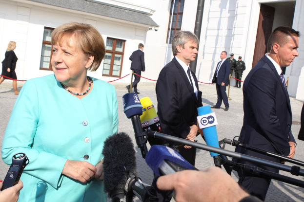 Bundeskanzlerin Angela Merkel bei einer Pressekonferenz im Kanzleramt in Berlin, umgeben von Menschen mit Mikrofonen und Gebäuden im Hintergrund.