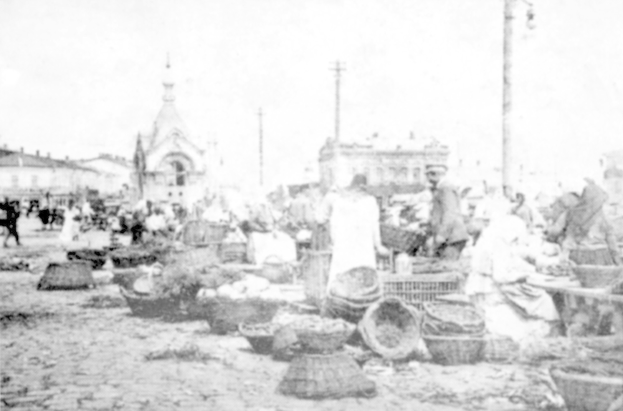 Schwarz-weiß-Foto eines belebten Marktes im alten Stadtzentrum von St. Petersburg mit Menschen, die sitzen und stehen, mit Körben und Gegenständen, umgeben von Gebäuden und Pfählen unter einem sichtbaren Himmel.