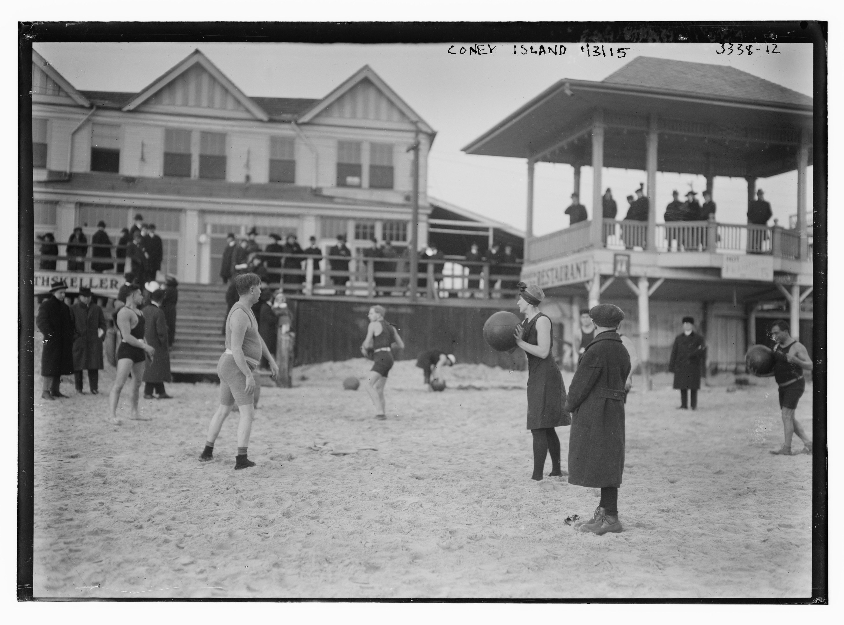 Schwarzes und weißes Foto von Menschen, die Fußball am Strand spielen, mit Gebäuden und Himmel im Hintergrund.