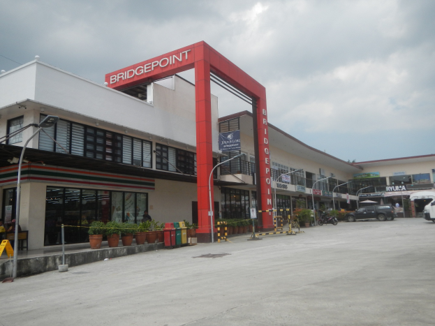 Tankstelle in den Philippinen mit Gebäuden, Fahrzeugen, Straßeninfrastruktur und Grünfläche unter einem bewölkten Himmel.