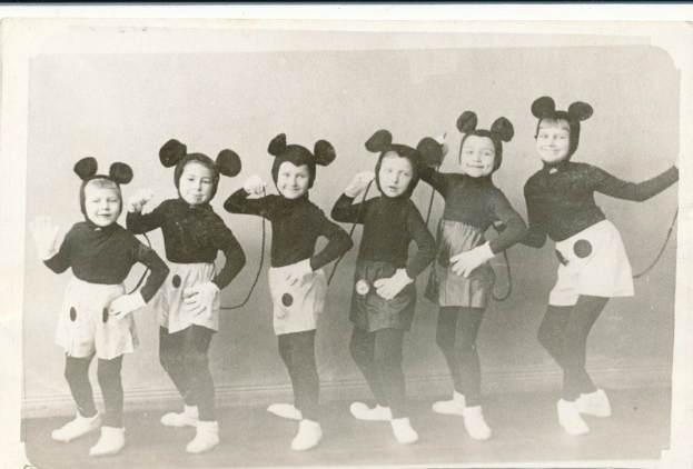 Eine Gruppe von Kindern in schwarzen und weißen Mickey-Maus-Kostümen, die für ein Foto in einem schwarzen und weißen Rahmen posieren, tragen passende Mickey-Maus-Ohren und Schuhe.