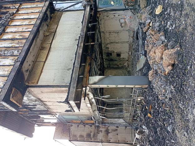 Verschmorte Überreste eines durch Feuer beschädigten Gebäudes mit Schutt auf dem Boden unter einem klaren Himmel.
